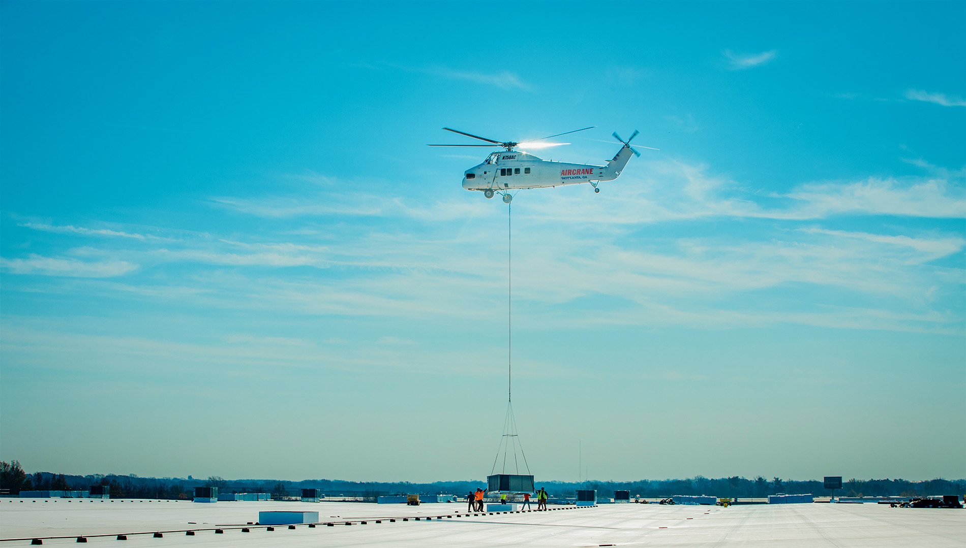 Drone photo of a helicopter lowering an air conditioning unit on a warehouse roof